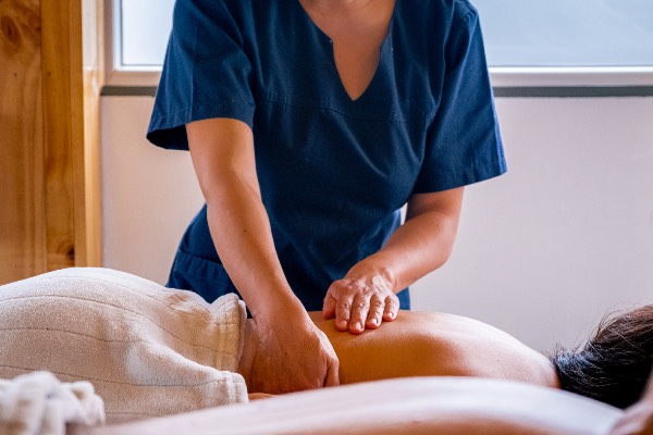 A photo of a female massage therapist in a blue shirt working on a client