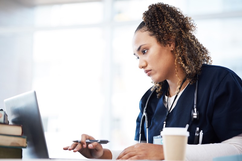 This is a stock photo of a young woman in scrubs working intently at a laptop computer. This image is for decorative purposes only.